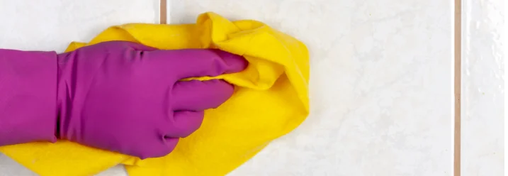 Hand in lila Handschuh reinigt Fliesen mit Tuch